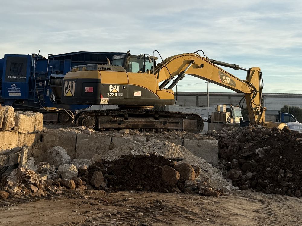 Escavatore CAT 323D su un cumulo di macerie davanti al frantoio