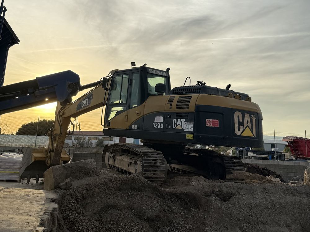 Escavatore CAT 323D al tramonto accanto al frantoio