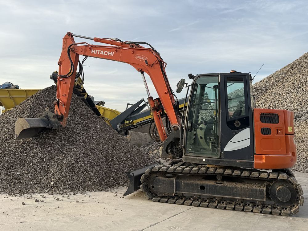 Escavatore Hitachi arancione con lama davanti a un cumulo di ghiaia